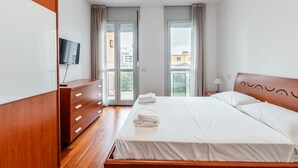 A bedroom with a wooden bed, a TV on the wall, and a balcony with curtains. - Casa Barbara, modern and peaceful with balcony (Milano)