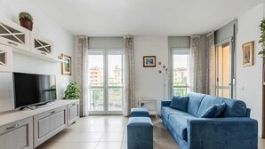 A modern living room with a flat-screen TV, a blue sofa, and a balcony with curtains. - Casa Barbara, modern and peaceful with balcony (Milano)
