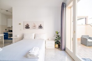 A modern hotel room with a neatly made bed, a small bedside table with a lamp, a potted plant, and a view of the outdoor balcony. - Savena Terrace Apartment, in the heart of San Lazzaro (San Lazzaro di Savena)