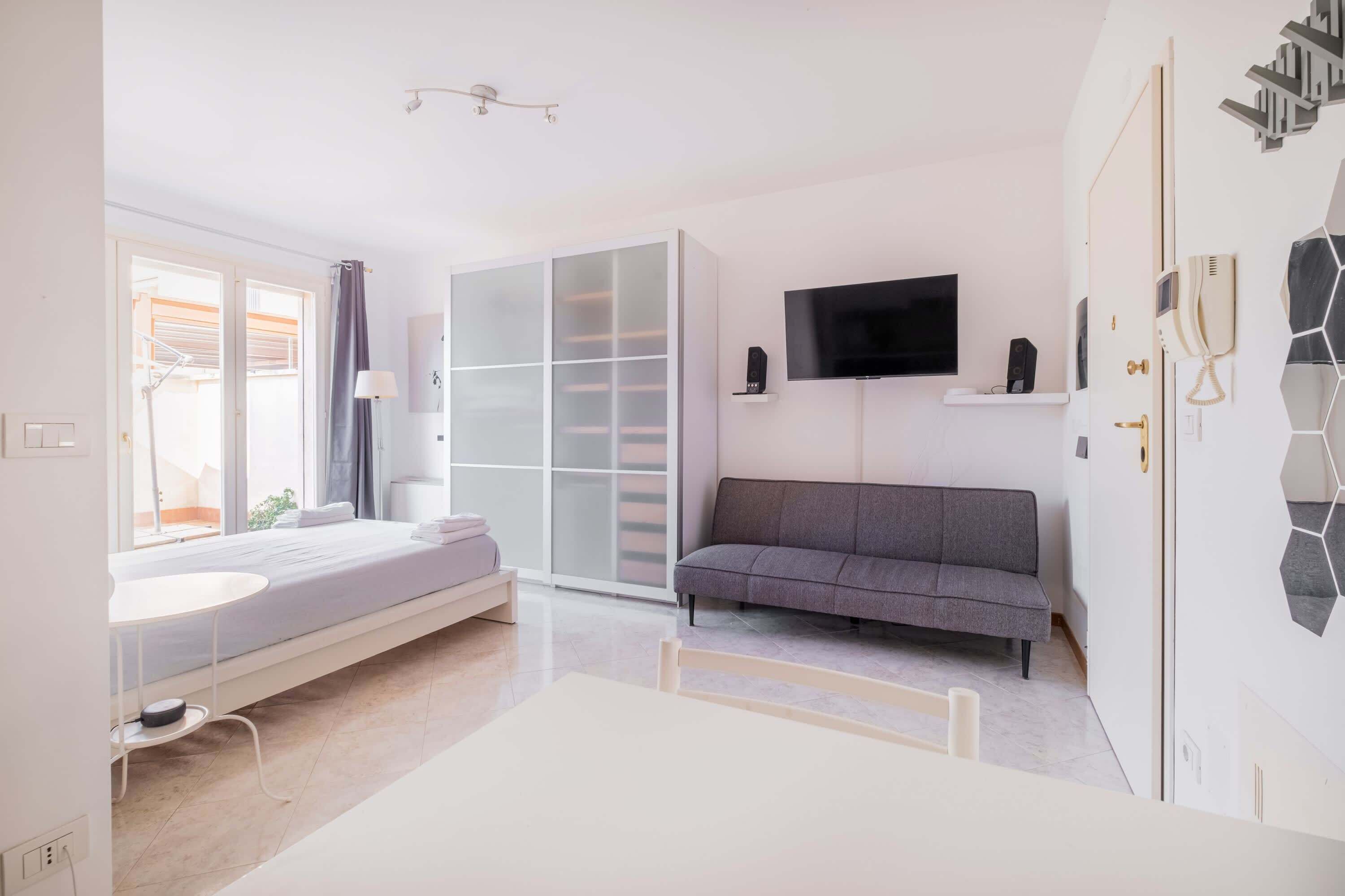 A modern bedroom with a bed, a sofa, a TV, and a wardrobe.