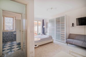 A bedroom with a bed, a sofa, a TV, and a bathroom with a shower and toilet. - Savena Terrace Apartment, in the heart of San Lazzaro (San Lazzaro di Savena)