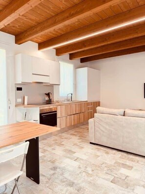 A modern kitchen with wooden beams, white cabinets, a wooden countertop, and a beige sofa.