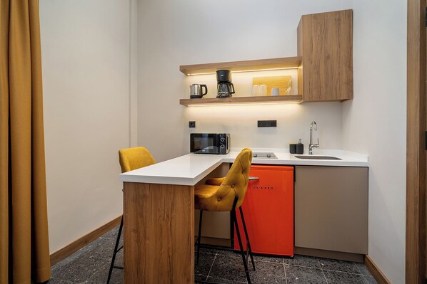 A compact kitchenette with a white countertop, a microwave, a coffee maker, a sink, and a red cabinet.