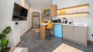 Une cuisine compacte équipée d’une machine à café, d’un grille-pain et d’un évier. On y trouve une chaise jaune et un lave-vaisselle bleu.