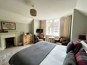 A bedroom with a large bed, a fireplace, a television, and a window with curtains.