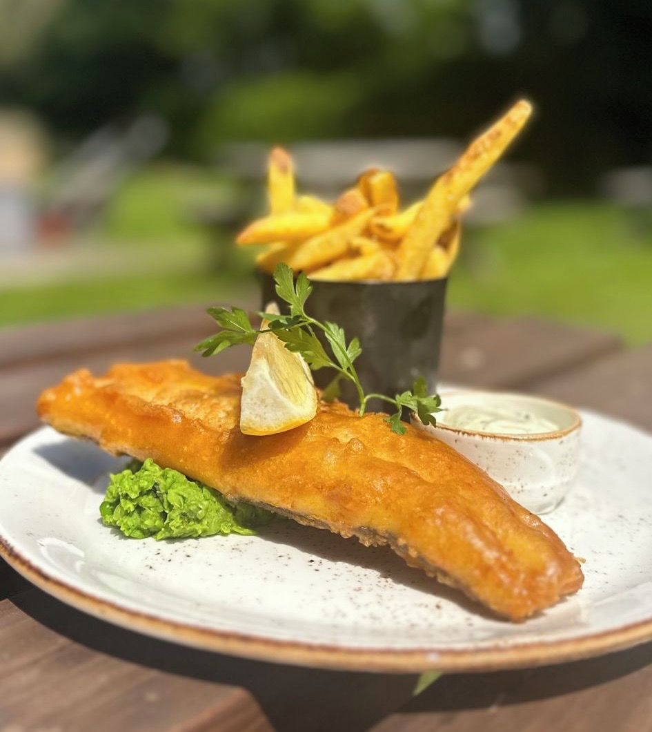 A plate with a piece of fish and chips, green sauce, and a small cup of sauce.