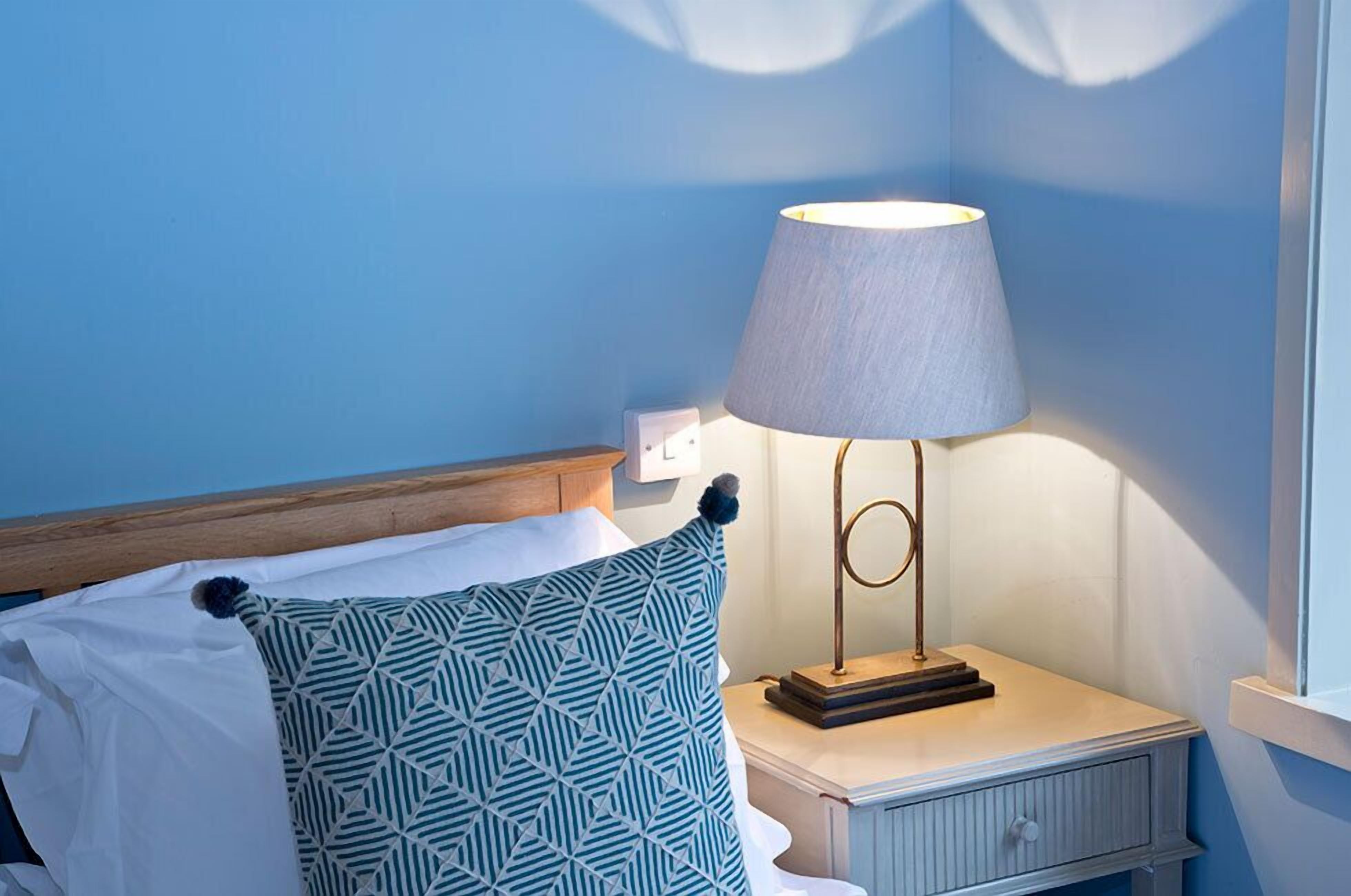 A neatly made bed with a geometric patterned pillow, a bedside lamp, and a nightstand with a small drawer.