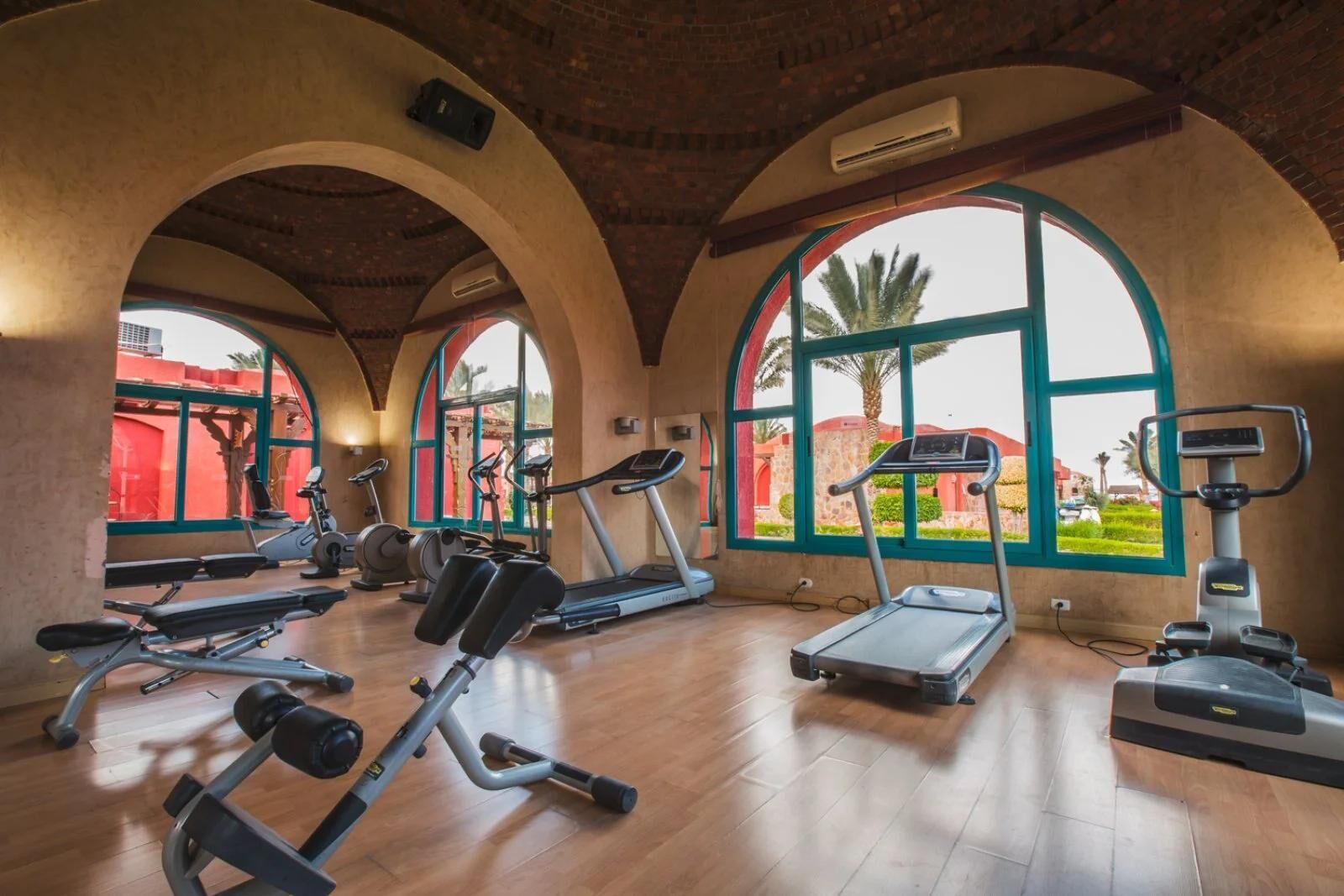A gym with multiple exercise machines, large arched windows, and a brick ceiling.