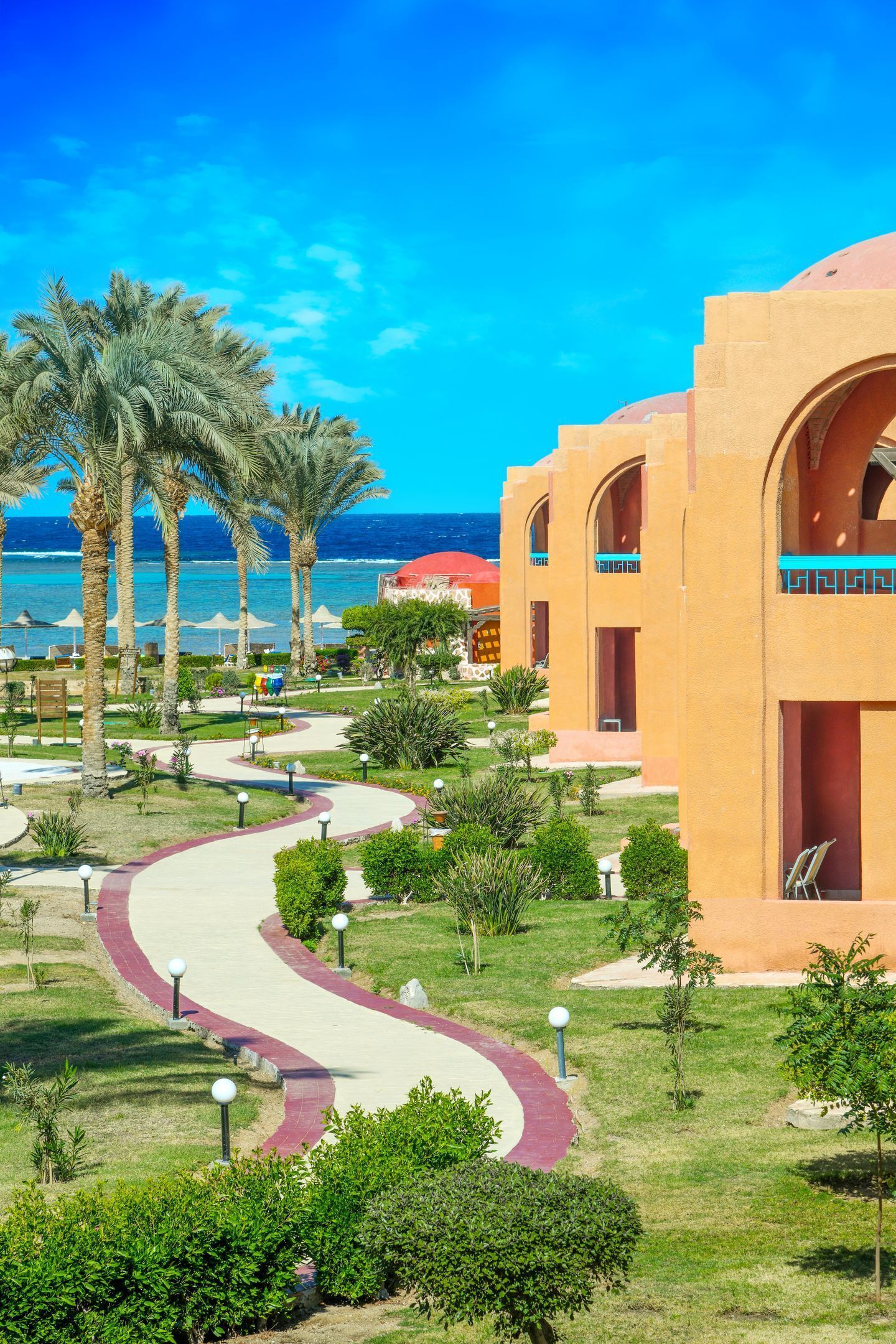 A resort with a curved pathway, palm trees, and a view of the ocean.