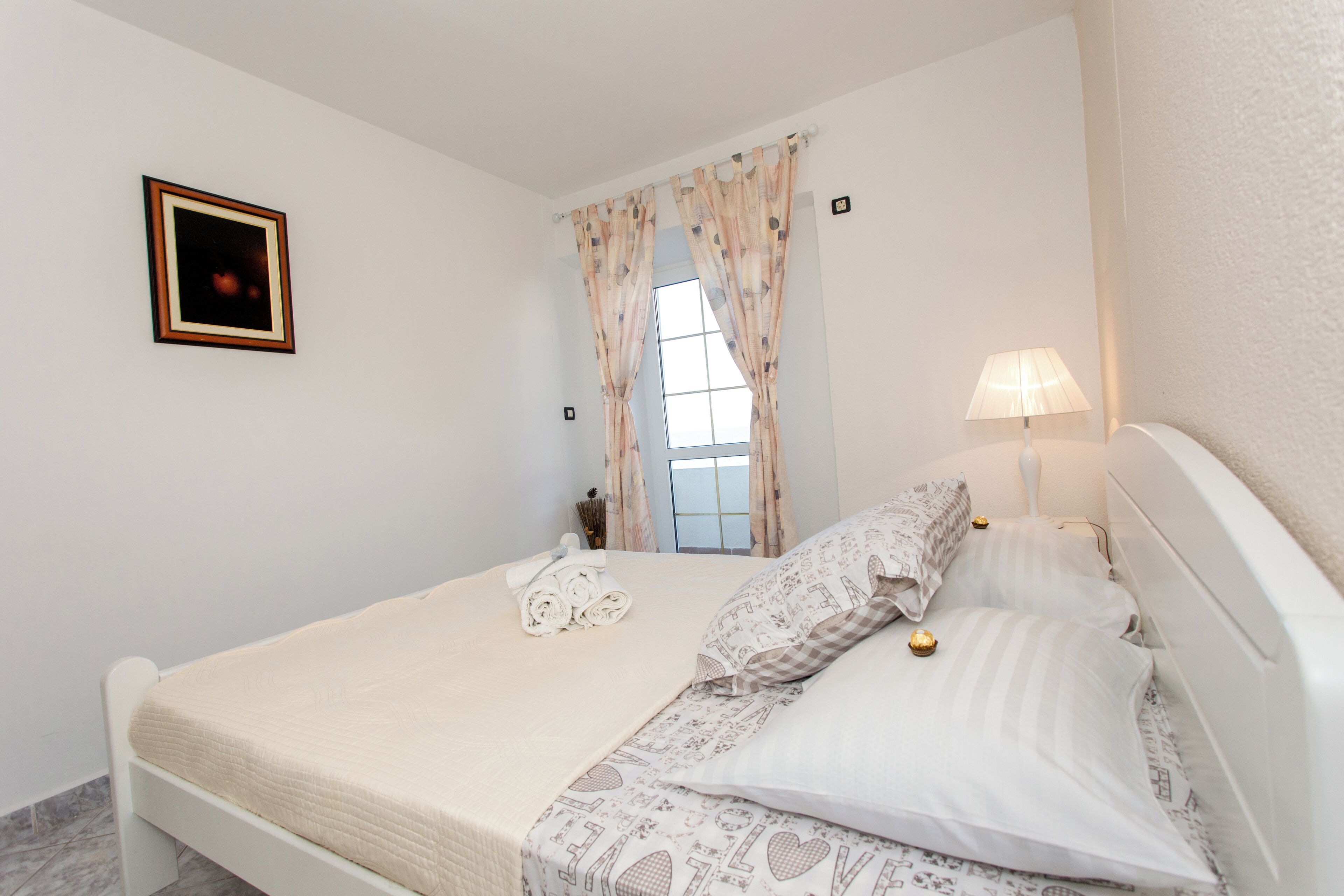A neatly made bed with a quilted cover, a bedside lamp, and a window with curtains.