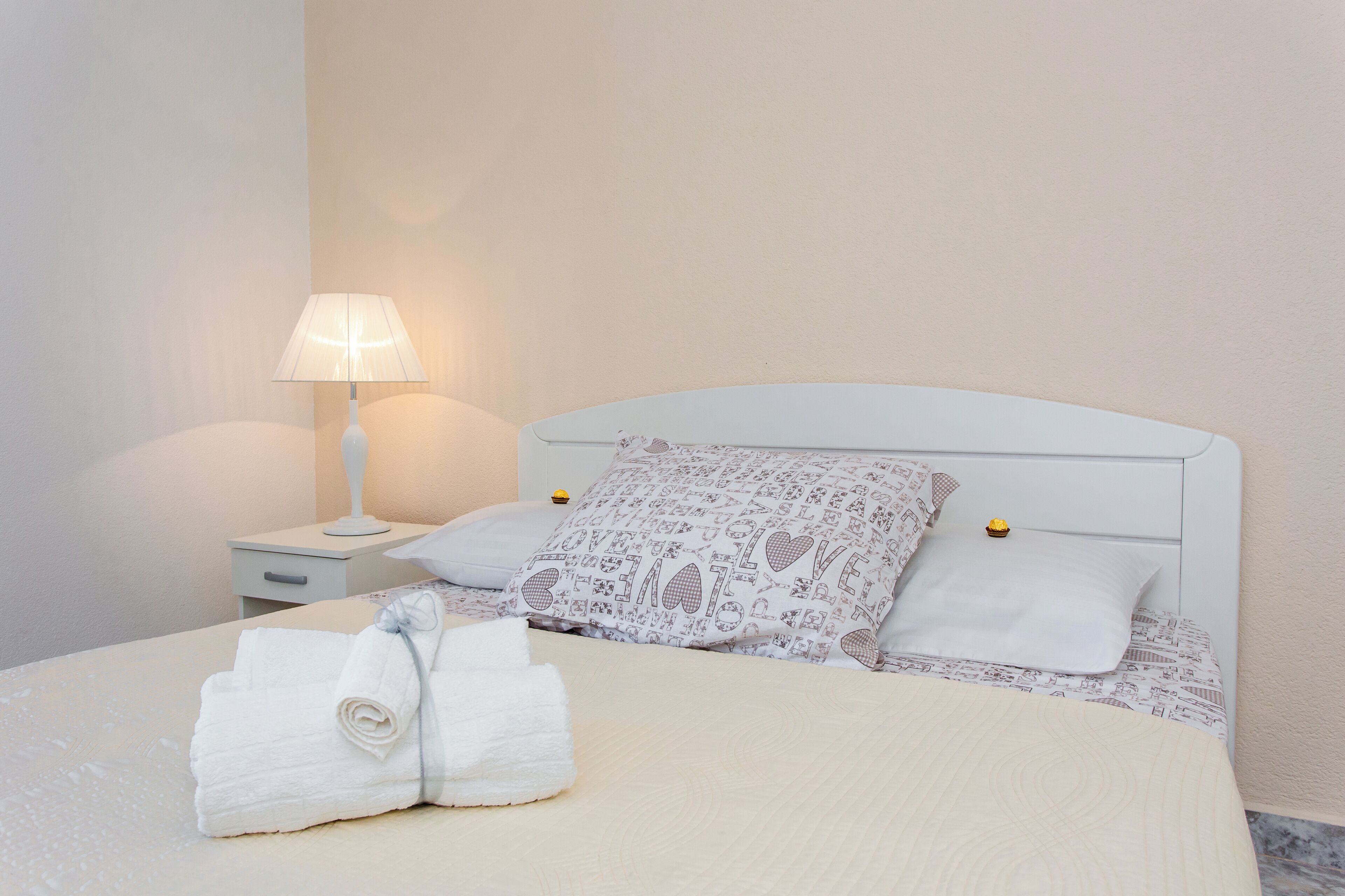 A neatly made bed with a patterned pillow, a rolled towel, and a bedside lamp.