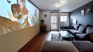 Un salon doté d’un grand écran de projection mural, d’un canapé de couleur sombre, d’une table basse en verre et d’un plancher en bois.