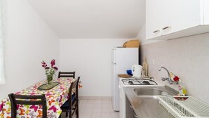 A compact kitchen with a gas stove, sink, and white cabinets. A dining table with chairs and a floral tablecloth is visible. - Apartments Sutvid (Janjina)