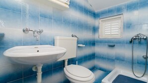 A bathroom with blue-tiled walls, a white sink, toilet, and a shower. - Apartments Sutvid (Janjina)