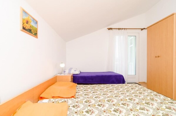 A bedroom with two beds, a wooden wardrobe, a nightstand with a lamp, and a window with curtains.