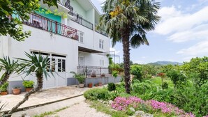 A two-story building with a balcony, surrounded by potted plants and a garden with pink flowers. - Apartments Sutvid (Janjina)