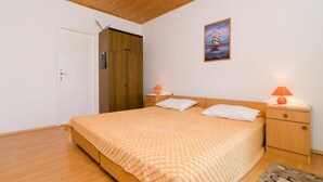 A bedroom with a wooden ceiling, a bed with a beige blanket, two bedside tables with lamps, a door, and a wall-mounted picture. - Apartments Sutvid (Janjina)