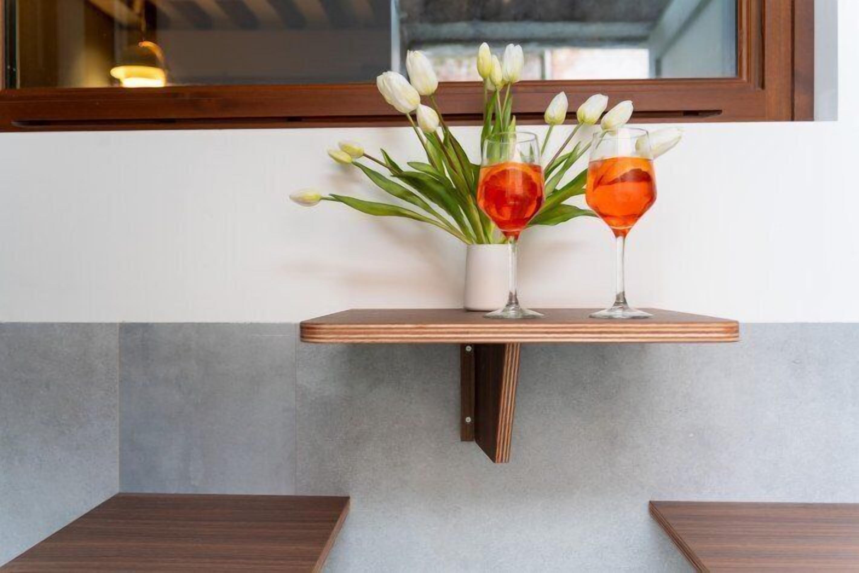 A wooden shelf with a vase of white tulips and two glasses of red wine.