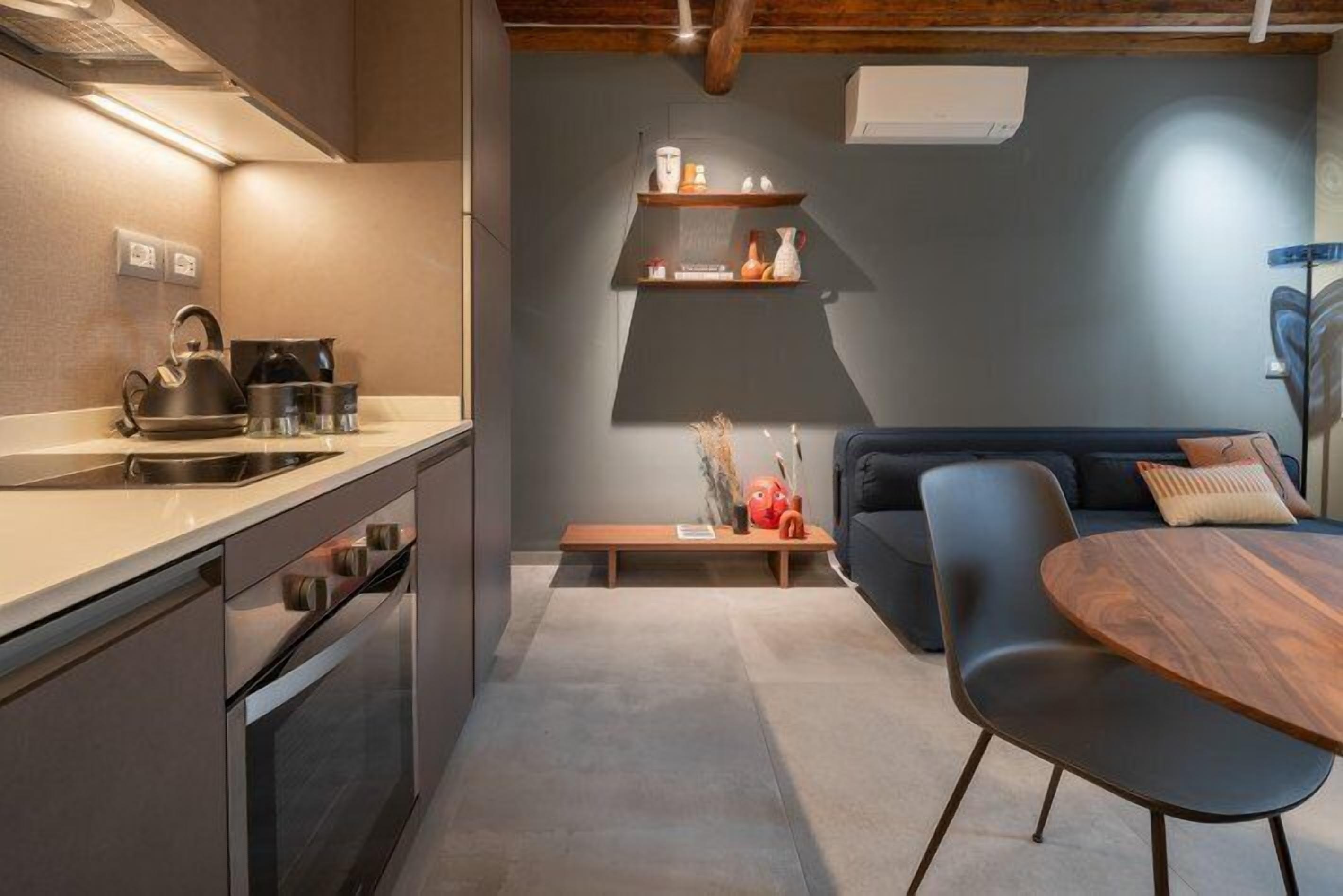 Una cocina moderna con horno integrado y un comedor con mesa redonda de madera y una silla azul.