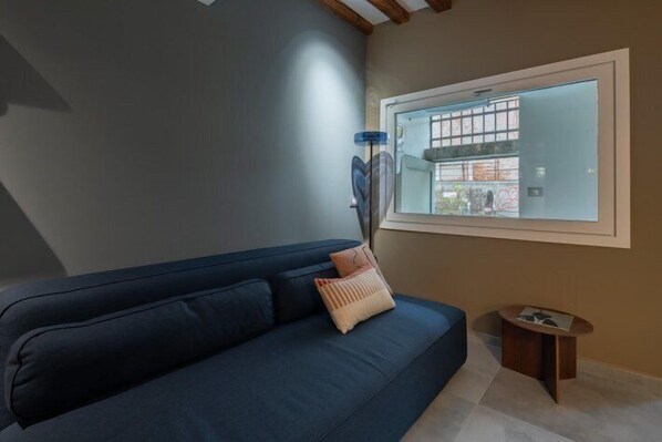 Un salon moderne avec un canapé bleu foncé, une petite table d’appoint en bois et une fenêtre donnant sur l’extérieur.