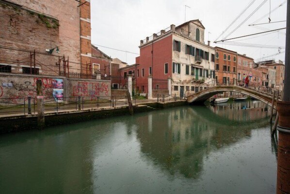 A canal with a bridge, buildings with graffiti, and a person walking. - Venice Jewel Canal View by Wonderful Italy (Venice)