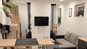 A modern living room with a wooden floor, a grey sofa, a coffee table, and a TV mounted on the wall. - Monteurwohnung Inkl. Wlan, Smart-tv, Küche, Waschmaschine, Parkplatz (Roding)