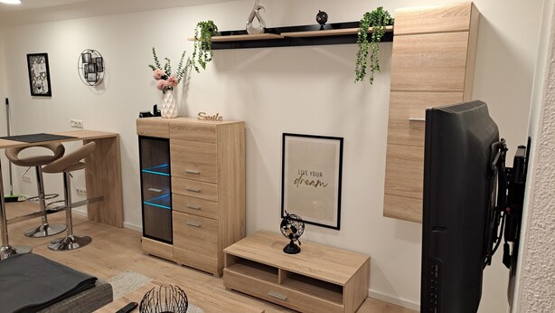 A modern living room with a wooden cabinet, a desk, a chair, and a television. - Monteurwohnung Inkl. Wlan, Smart-tv, Küche, Waschmaschine, Parkplatz (Roding)