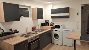 A compact kitchen with a gas stove, a washing machine, a microwave, and a coffee maker. - Monteurwohnung Inkl. Wlan, Smart-tv, Küche, Waschmaschine, Parkplatz (Roding)