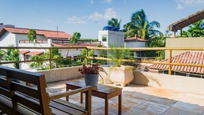 A rooftop terrace with wooden furniture, potted plants, and a view of neighboring buildings. - Casa Mar Self Jeri (Jijoca de Jericoacoara)