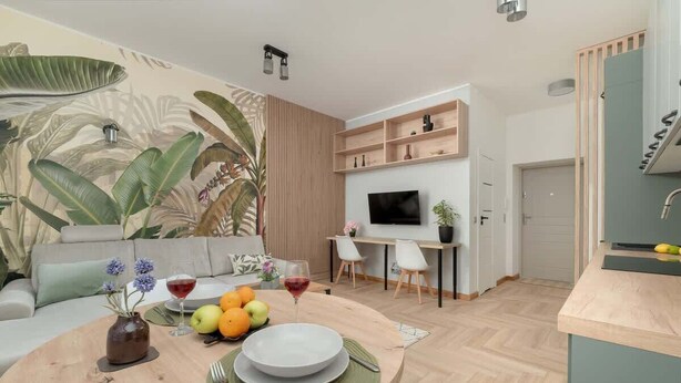 Una sala de estar moderna con un mural grande, una zona de comedor con una mesa redonda y una cocina con televisor y estanterías de madera.