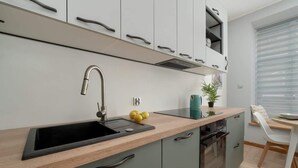 Una cocina moderna con un lavabo negro, horno empotrado y ventana con persianas.