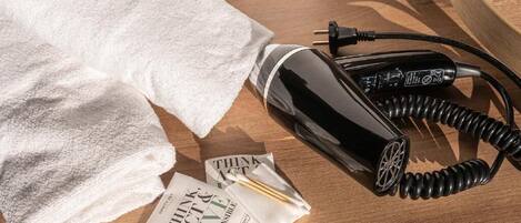 A neatly folded white towel, a black hairdryer, and a pamphlet on a wooden surface.