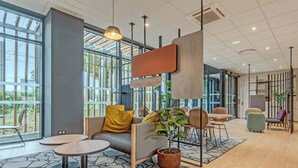 A modern interior with a sofa, coffee table, and chairs, large windows, and a hanging light fixture. - B&B Hotel Brest Porte De Gouesnou (Gouesnou)