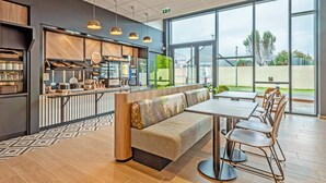 A modern cafe with a long counter, a seating area with a bench, and large windows offering a view of the outdoors. - B&B Hotel Brest Porte De Gouesnou (Gouesnou)
