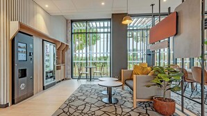 A modern hotel lobby with a seating area, a coffee machine, and large windows offering a view of the outdoors. - B&B Hotel Brest Porte De Gouesnou (Gouesnou)