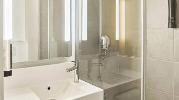 Un baño moderno con un lavamanos blanco, un espejo grande y un box de ducha de vidrio.