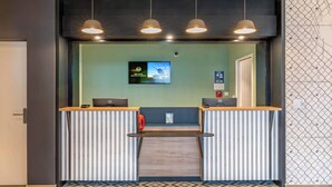 A reception desk with a flat-screen TV, a red telephone, and a wooden counter. - B&B Hotel Brest Porte De Gouesnou (Gouesnou)