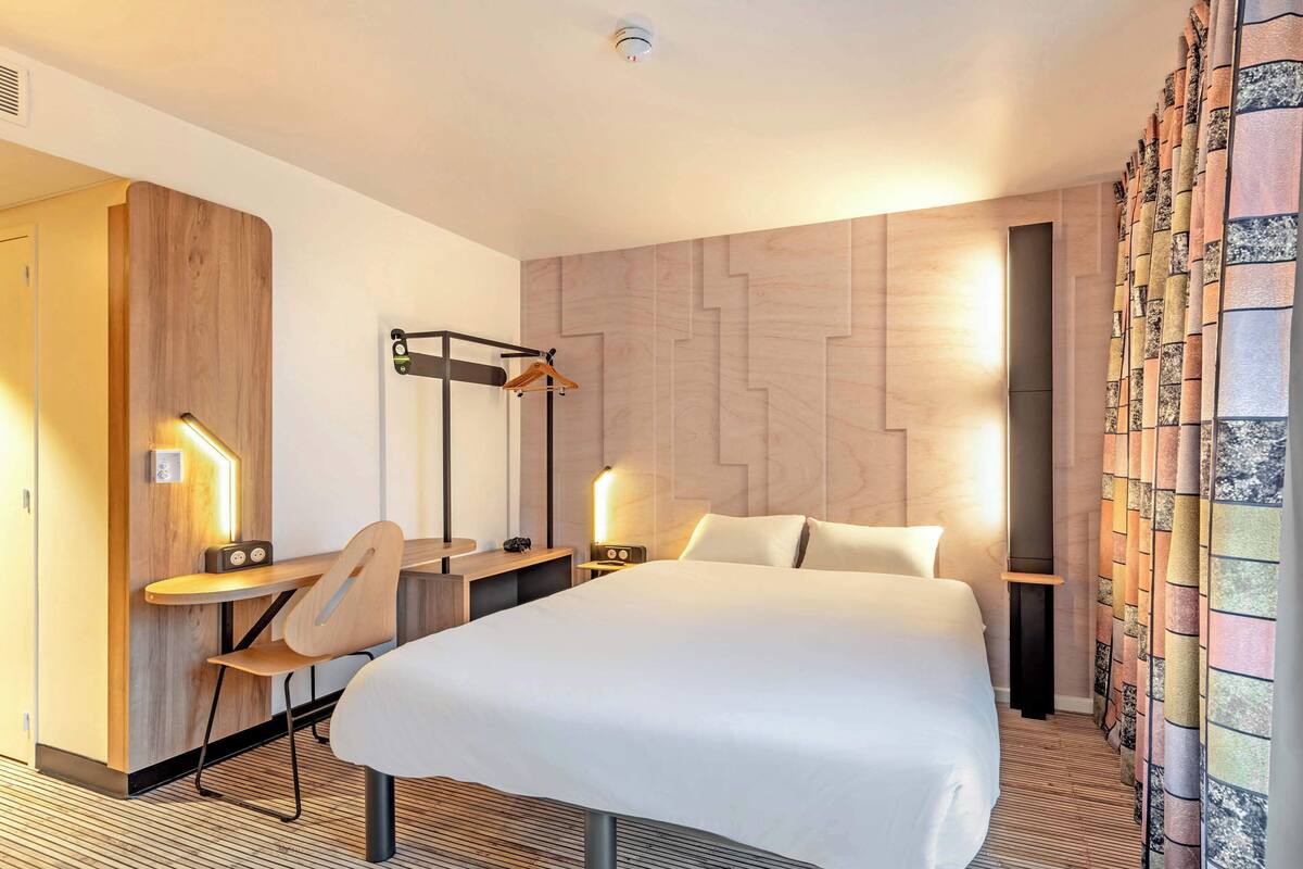 Moderni hotellihuone, jossa on suuri sänky, työpöytä tuolilla, pöytävalaisin ja seinälle asennettu televisio.