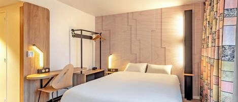 Een moderne hotelkamer met een groot bed, een bureau met stoel, een bureaulamp en een tv aan de muur.