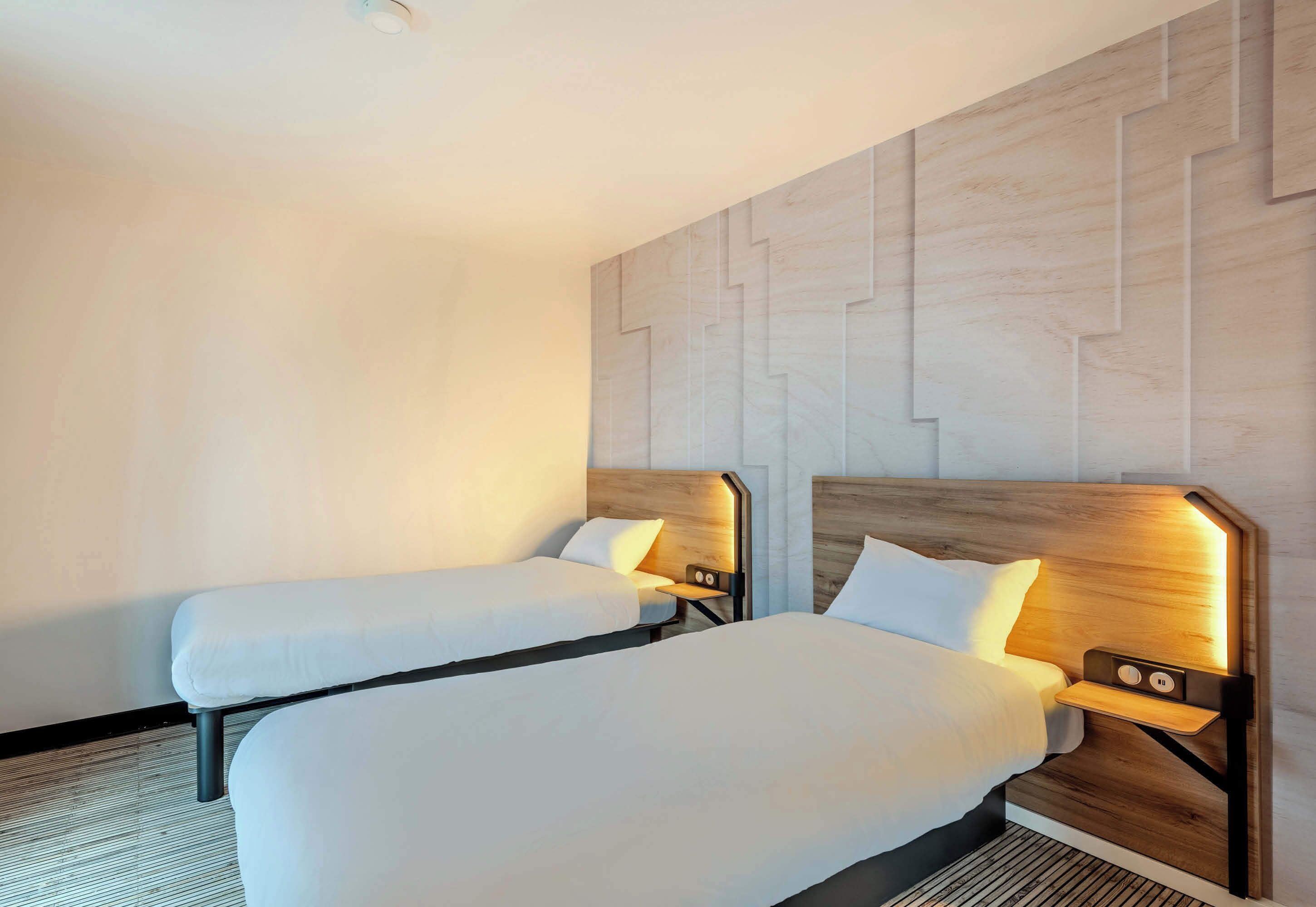 Ein Hotelzimmer mit zwei Einzelbetten, Holz-Kopfteilen, Nachttischen inklusive Lampen und einer Wand mit Muster.