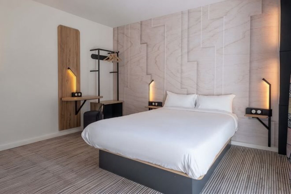 Une chambre d’hôtel moderne dotée d’un grand lit, d’une tête de lit en bois et d’un éclairage intégré.