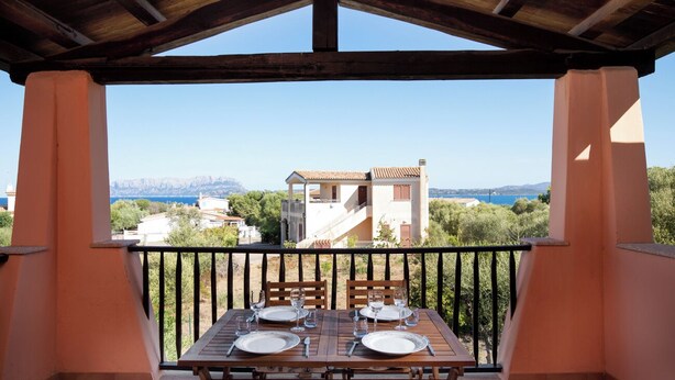 Un balcón con una mesa lista para dos personas, con vista a un paisaje montañoso.