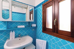 A bathroom with a white sink, blue tiled walls, a wooden cabinet with a mirror, and a towel on the floor. - Casa Le Sirene by Wonderful Italy (Olbia)