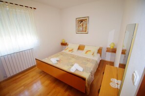 A hotel room with a wooden bed, a bedside table with a lamp, a radiator, and a painting on the wall. - Cozy 2-bedroom apartment with parking, AC in delightful village Valbandon (Valbandon)