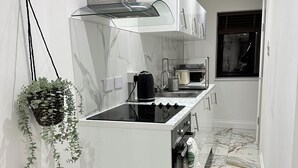 A modern kitchen with a central island, a hanging plant, and a window with blinds.