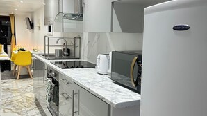 A modern kitchen with a white refrigerator, stainless steel appliances, and a marble countertop.