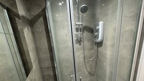 A glass-enclosed shower with a handheld showerhead and a wall-mounted faucet.