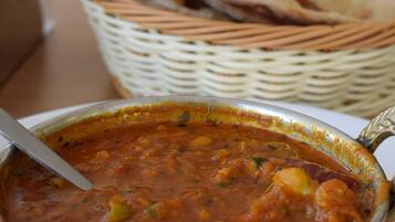 Un tazón de dal con una cuchara, una cesta de naan y una cesta tejida al fondo.