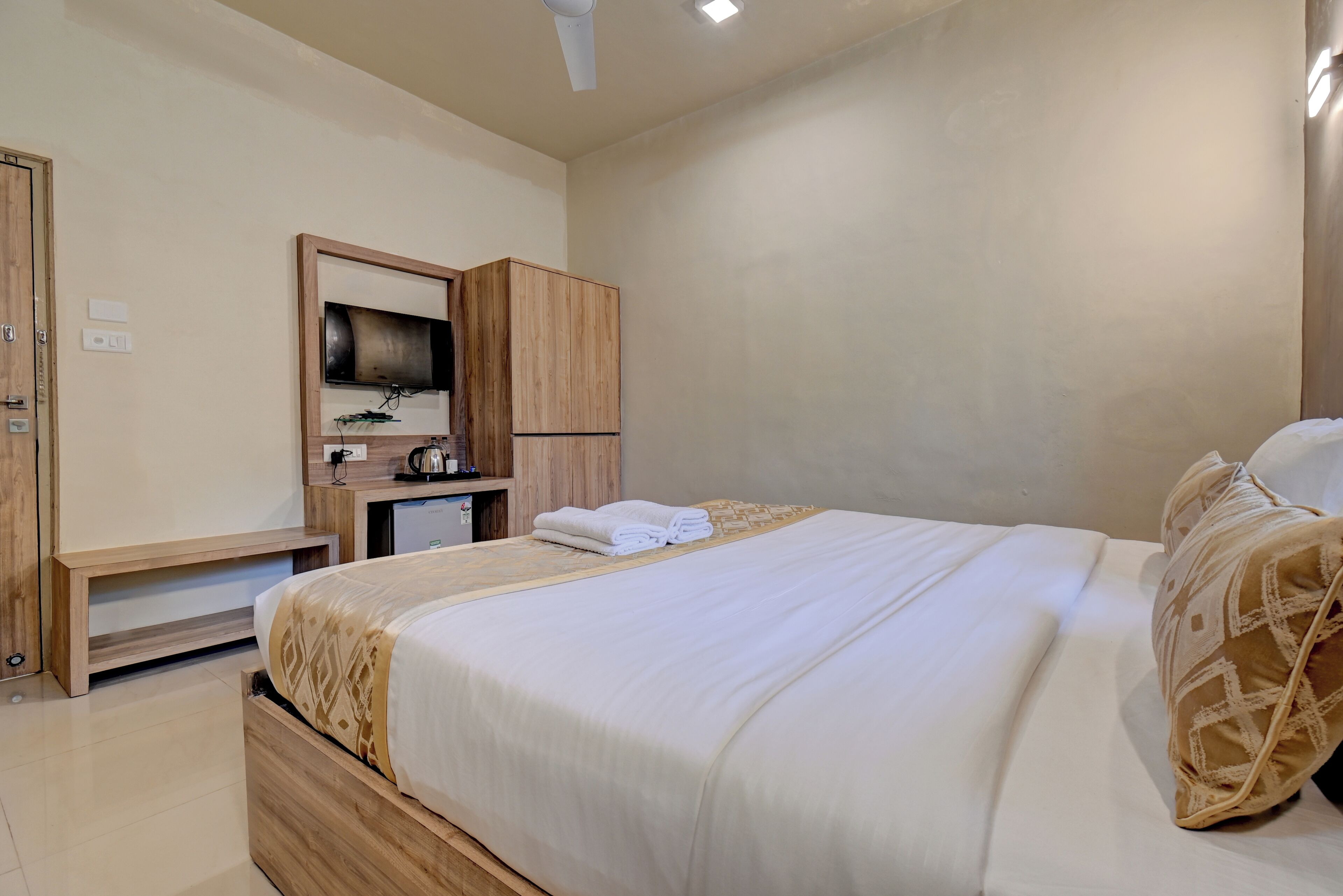 A bedroom with a bed, wooden wardrobe, TV, and a small desk with a kettle.