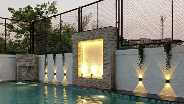 Ein Schwimmbad mit Steinmauer und Fenster aus Glasbausteinen, umgeben von einem Metallzaun und Grünpflanzen.